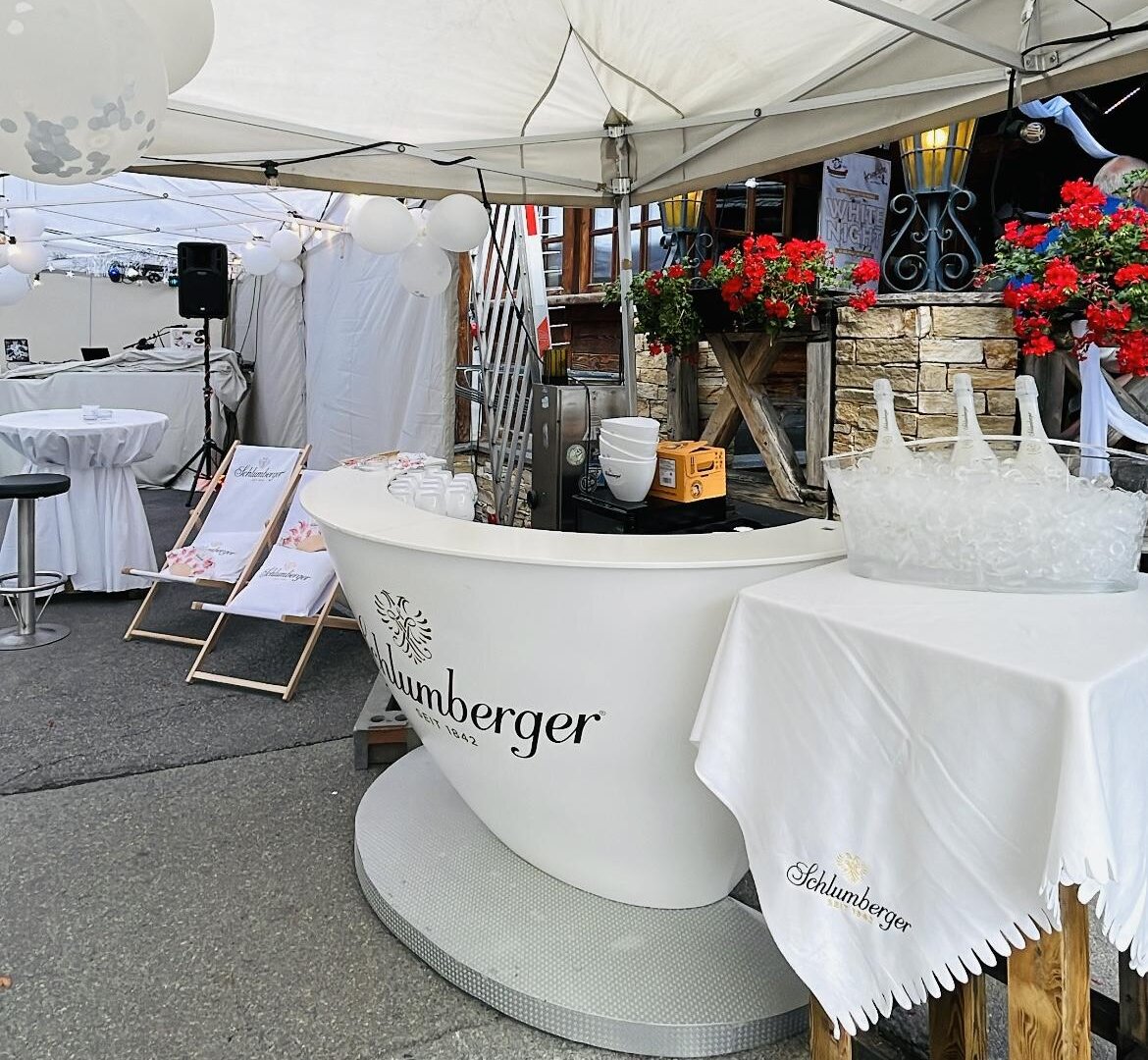 Ein Außenzelt mit einem eleganten Empfangstresen und Blumenarrangements. Der Bereich scheint für eine Veranstaltung oder Feier vorbereitet zu sein.