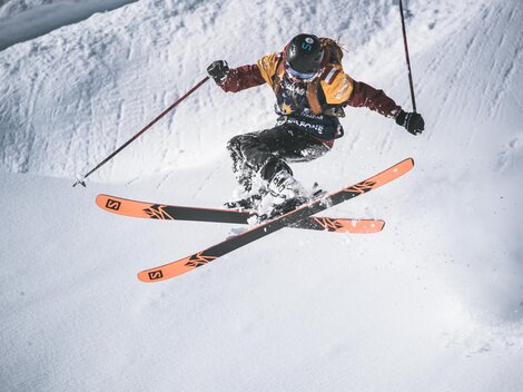 Ein Skifahrer springt über einen schneebedeckten Hang. Er trägt eine bunte Skiausrüstung und zeigt eine beeindruckende Technik.