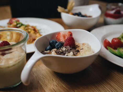 A beautiful table with various breakfast dishes. A bowl of oatmeal, fresh berries, and chocolate is visible in the foreground.