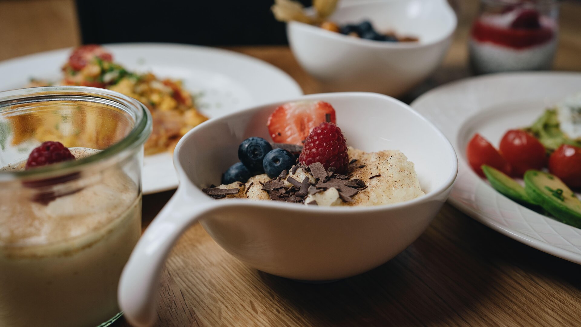 A beautiful table with various breakfast dishes. A bowl of oatmeal, fresh berries, and chocolate is visible in the foreground.