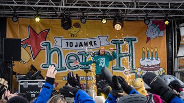 An artist stands on stage and captivates the audience. In the background, decorations for an anniversary celebration can be seen.