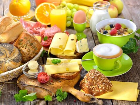 A hearty breakfast with various types of bread, colorful fruit, and drinks. Additionally, there is cheese and yogurt in appetizing bowls.
