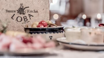 Ein dekoratives Restaurantmenü mit dem Namen "Loba" ist im Vordergrund zu sehen. Im Hintergrund befinden sich verschiedene kleine Gerichte und Snacks.