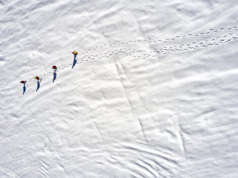 Vier Personen gehen über eine schneebedeckte Fläche. Ihre Spuren sind im frischen Schnee deutlich sichtbar.