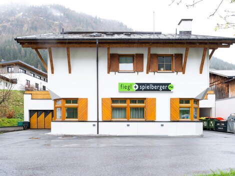 A modern building with a white exterior paint and wood cladding. The logo of "fiegL spielberger" is prominently displayed above the entrance.