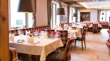 Ein stilvolles Restaurant mit eleganten Tischen und karierten Stühlen. Große Fenster sorgen für helles Licht und eine einladende Atmosphäre.
