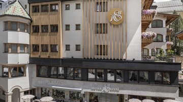 Ein modernes Hotelgebäude mit einem ansprechenden Design. Im Vordergrund sind Sitzgelegenheiten und dekorative Pflanzen zu sehen.