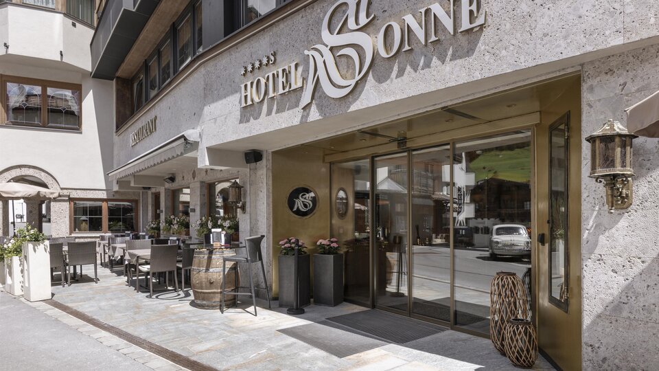 Der Eingang zum Hotel Sonne ist stilvoll gestaltet und einladend. Es gibt Sitzgelegenheiten im Freien und eine moderne Fassade.