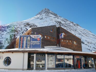 Ein modernes Gebäude vor einem schneebedeckten Berg. Der klare Himmel und die Winterlandschaft schaffen eine malerische Aussicht.