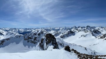 Eine beeindruckende Berglandschaft mit schneebedeckten Gipfeln und einem klaren blauen Himmel. Die Sicht ist weit und atemberaubend.