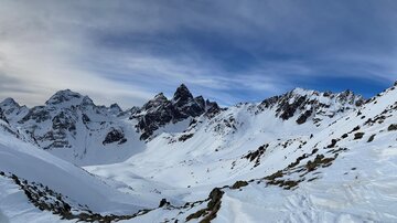 Eine beeindruckende Berglandschaft mit schneebedeckten Gipfeln und einem blauen Himmel. Die Sonne scheint über die winterliche Szene.
