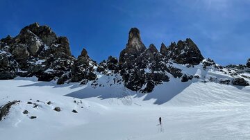 Eine winterliche Landschaft mit schneebedeckten Bergen und klarem, blauem Himmel. Eine Person wandert durch den Schnee.