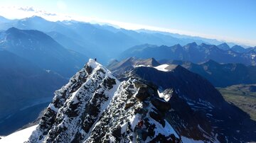 Eine beeindruckende Berglandschaft mit schneebedeckten Gipfeln und tiefen Tälern. Der klare Himmel lässt die majestätische Schönheit der Alpen erstrahlen.