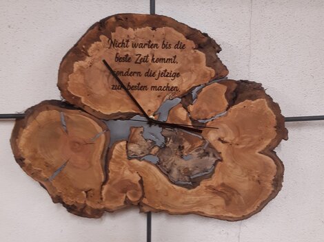 Eine dekorative Wanduhr aus Holz mit einer einzigartigen Form. Darauf steht der Spruch: "Nicht warten bis die beste Zeit kommt, sondern die jetzige zu nutzen machen."