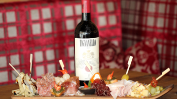 Ein stilvolles Arrangement aus verschiedenen Wurst- und Käsesorten auf einem Holzbrett, umgeben von frischen Beilagen. Dazu eine Flasche Rotwein, die eine gemütliche Atmosphäre schafft.
