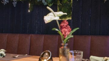 Ein stilvolles Restaurant mit einer Holztafel und elegantem Geschirr. Im Hintergrund leuchtet ein neonfarbener Schriftzug mit dem Namen „Prenner“.
