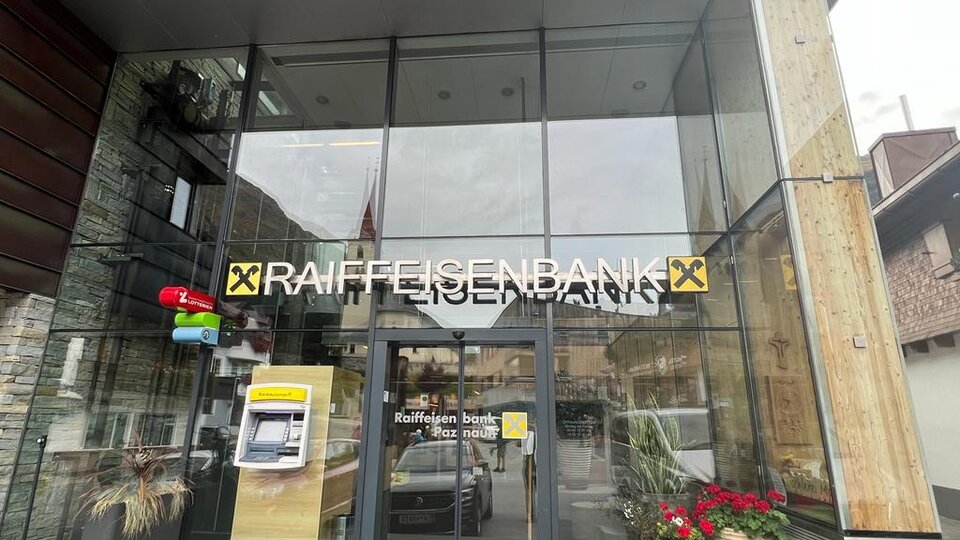 A modern bank building with large glass windows. The entrance belongs to Raiffeisenbank and is decorated with plants.