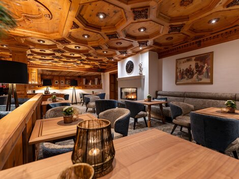 Ein gemütliches Restaurant mit Holzvertäfelung und eleganten Möbeln. Es gibt Tische, lichtdurchflutete Bereiche und einen Kamin im Hintergrund.