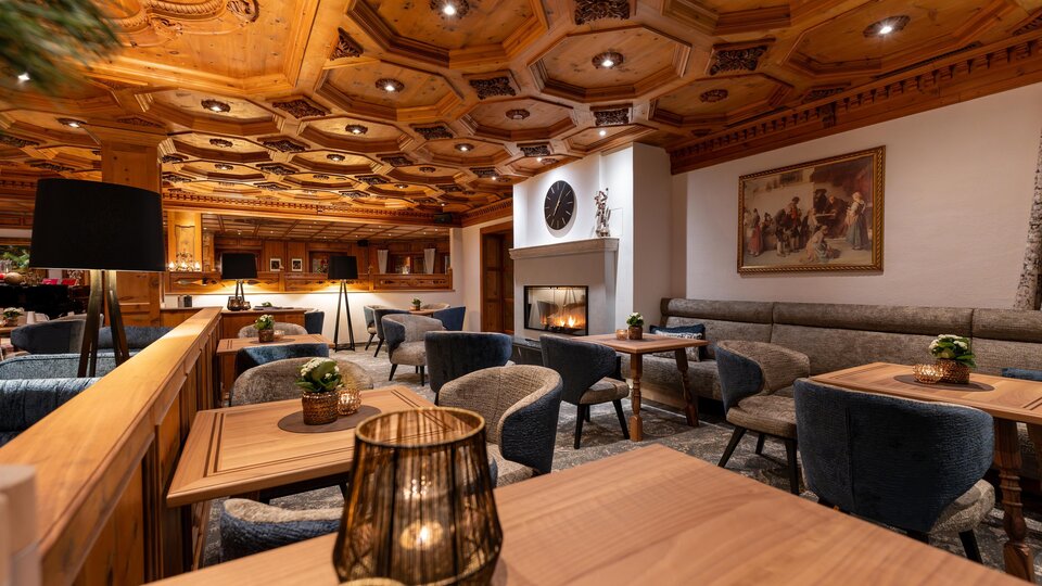 Ein gemütliches Restaurant mit Holzvertäfelung und eleganten Möbeln. Es gibt Tische, lichtdurchflutete Bereiche und einen Kamin im Hintergrund.