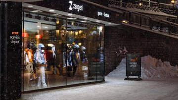 A sports store with a display window featuring ski clothing. Outside, snow is on the ground and it is illuminated.