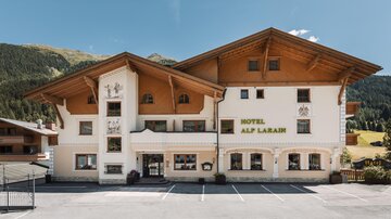 A charming hotel with traditional alpine architecture and clear lines.  
Surrounded by mountains and green terrain, it offers an inviting atmosphere.