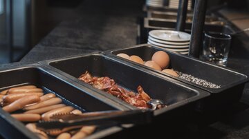 A buffet with various breakfast ingredients. There are sausages, bacon, eggs, and spices.