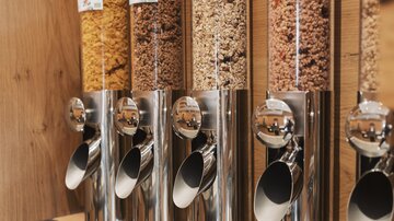 A modern cereal bar with various types of grains in transparent dispensers. The dispensers are made of stainless steel and provide a practical way to fill cereal.