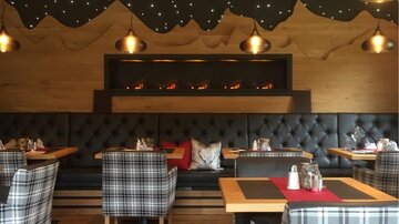 A stylish restaurant with cozy, checkered seating and warm wooden decor. The soft lighting creates an inviting atmosphere.