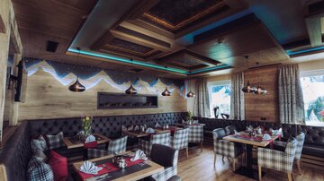 A cozy restaurant with wooden elements and stylish furniture. The walls are decorated with an artistic mountain landscape.