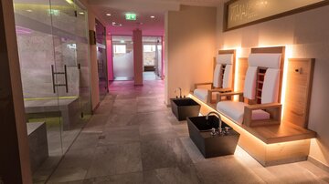 An elegant spa area with bright walls and stylish seating. Relaxing foot baths are visible in the background.