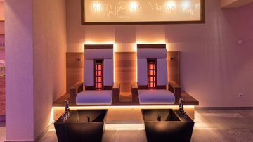 An elegant wellness area with two comfortable loungers and dark sinks. Soft lighting creates a relaxing atmosphere.
