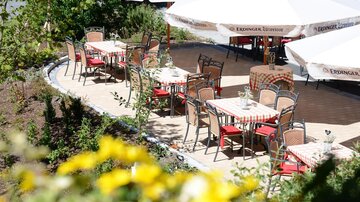 A cozy outdoor area with tables and chairs, surrounded by plants. Umbrellas provide shade for the guests.