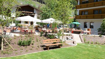 A beautiful garden with seating areas and sun umbrellas. In the background, a building is visible that creates a relaxing atmosphere.