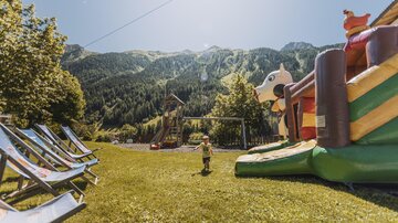 A beautiful playground with a large bounce castle and a breathtaking view of the mountains. In the foreground, there are deck chairs on the green meadow.