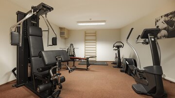 A modern gym with various training equipment. The room is well-lit and has carpet flooring.