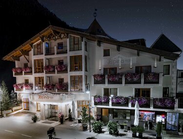 A beautiful hotel with blooming balcony plants and an inviting entrance area. The surroundings are quiet and the night has a clear starry sky.