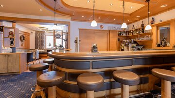 Eine gemütliche Bar mit Holzverkleidung und runden Hockern. Im Hintergrund sind Getränke und eine einladende Atmosphäre zu sehen.