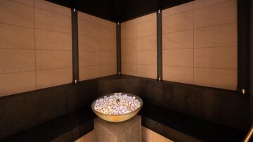 Ein eleganter Wellnessbereich mit dunklen Wänden und sanfter Beleuchtung. In der Mitte befindet sich eine Schale mit Steinen, die ein entspannendes Ambiente schaffen.