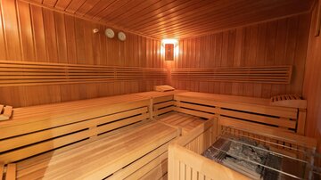 Eine gemütliche Sauna mit Holzvertäfelung und Bänken. Ein kleiner Ofen ist in der Ecke zu sehen.
