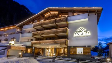 Ein modernes Hotelgebäude mit Holzverkleidung und beleuchteter Fassade in einer schneebedeckten Umgebung. Der Himmel ist in der Dämmerung, und die Atmosphäre ist einladend.