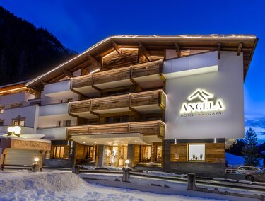 A modern hotel building with wooden cladding and a illuminated facade in a snow-covered environment. The sky is at twilight, and the atmosphere is welcoming.