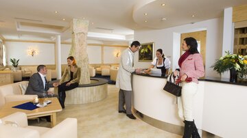 An elegant lounge with modern furniture and a reception desk. Guests are interacting casually with each other and with the staff.
