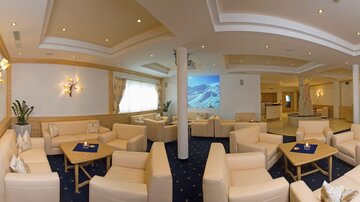 An elegant lounge with comfortable white sofas and stylish tables. On the wall, there is a presentation featuring a mountain landscape.