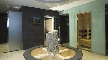 A modern wellness area with elegant glass walls. In the center stands a round stone element next to a sauna.