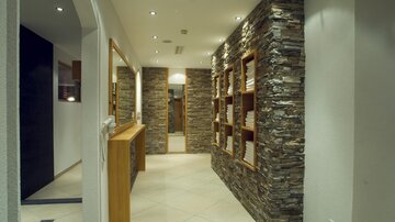 A modern hallway with stone walls and wooden shelves. The room is well-lit and has a friendly atmosphere.
