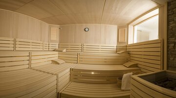 A calm sauna area with wooden benches and gentle lighting. A window provides daylight and a relaxing atmosphere.