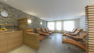A relaxing wellness area with loungers and warm light. The walls are clad in natural stone and there is a modern wooden paneling.