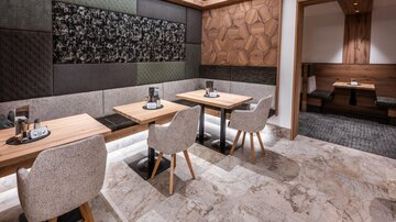 A modern restaurant with elegant tables and comfortable chairs. The walls are decorated with various textures and wooden panels.