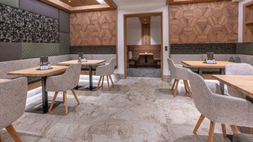 A modern restaurant with stylish tables and upholstered chairs. The walls are decorated with wood and colored panels, while the floor consists of various types of stone.