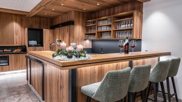 A modern kitchen with a wooden bar and elegant bar stools. On the counter are wine glasses and decorations for an inviting atmosphere.
